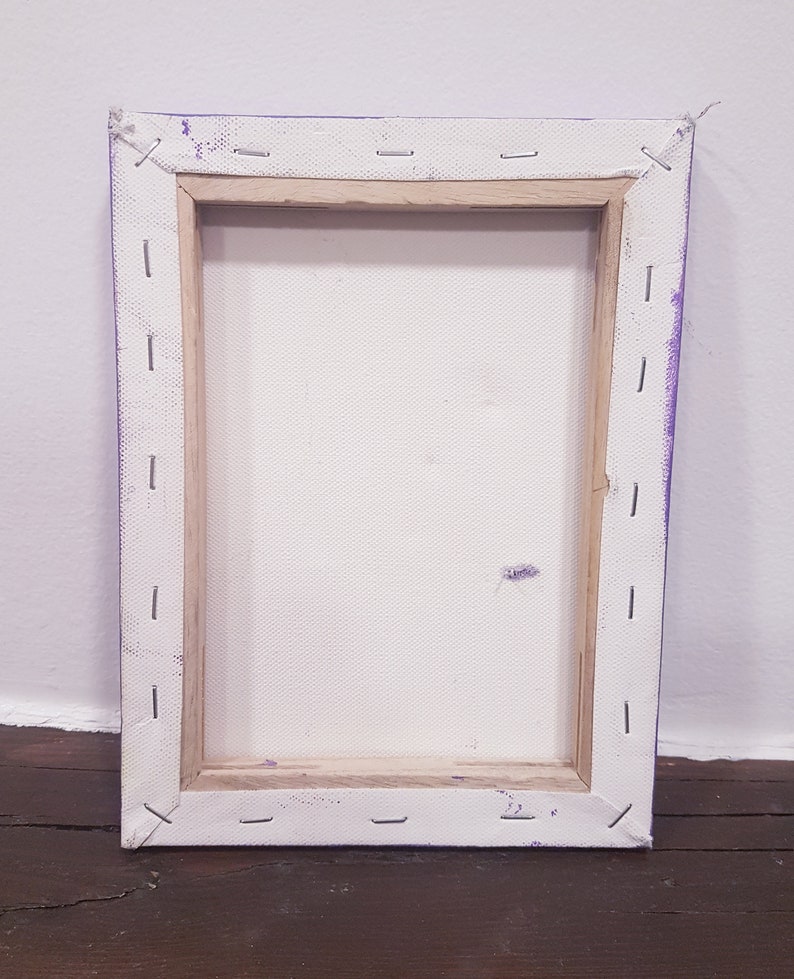 May include: Back of a rectangular canvas art piece. The canvas is stretched over a wooden frame and secured with staples. The edges are painted purple. The canvas is white and shows a few small marks.