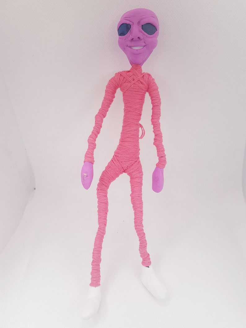May include: A pink yarn wrapped doll with a purple alien head and white shoes.