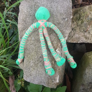 May include: A green and pink octopus toy with long, thin tentacles. The toy is made of fabric and has a soft, plush texture.