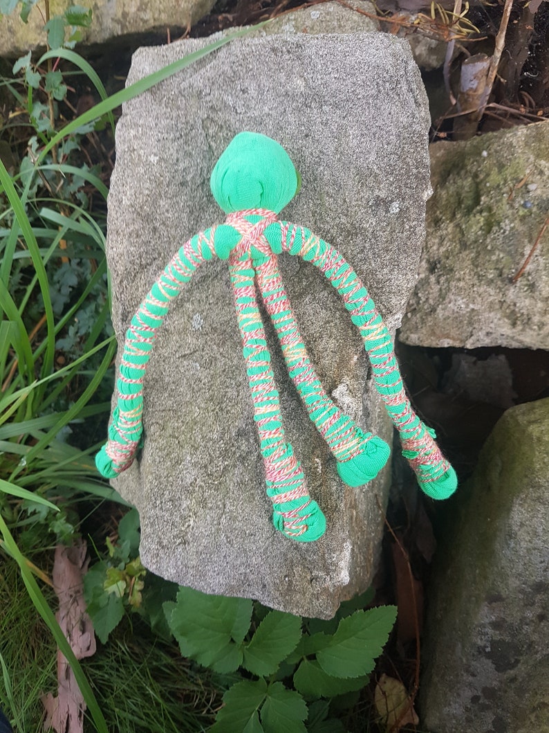 May include: A green and pink octopus toy with long, thin tentacles. The toy is made of fabric and has a soft, plush texture.