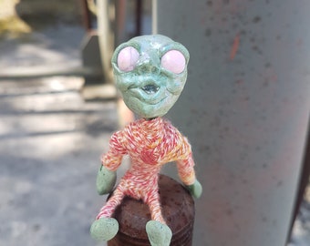 green alien doll with big brown eyes , disturbing and cute