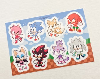May include: A sheet of stickers featuring various characters from the Sonic the Hedgehog video game series. The stickers include Sonic, Tails, Amy, Knuckles, Shadow, Rouge, Blaze, and Silver, set against a blue sky and a brown and tan ground.