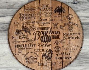 May include: A round, wooden bourbon barrel head with various bourbon distillery logos and the words "Kentucky Bourbon Trail" etched into the wood. The logos include "Jim Beam", "Buffalo Trace", and "Wild Turkey".