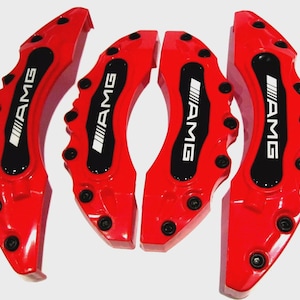 May include: Four bright red AMG brake caliper covers. Each cover has a black center section with the AMG logo in white. The covers are designed to fit over the brake calipers of a vehicle.