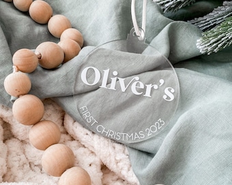 Könnte beinhalten: Ein runder, transparenter Weihnachtsbaumschmuck mit dem Text "Oliver's First Christmas 2023" in weißen Buchstaben.
