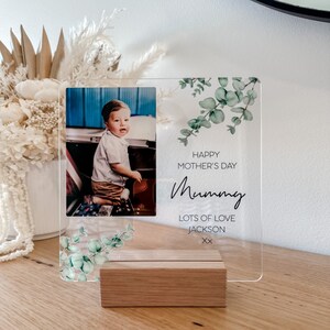 Puede incluir: Un marco de fotos de acr&iacute;lico transparente con una foto de un ni&ntilde;o peque&ntilde;o y un mensaje que dice "Happy Mother's Day Mummy Lots of Love Jackson xx". El marco est&aacute; decorado con un dise&ntilde;o de hojas de eucalipto.