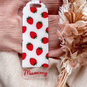 May include: A white bookmark with a red strawberry pattern and the word "Mummy" written in red on the bottom. The bookmark has a white ribbon attached to the top.