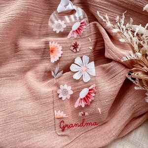 May include: A clear acrylic bookmark with a floral design and the word "Grandma" in red lettering. The bookmark is hanging from a white ribbon.
