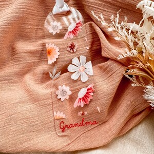 May include: A clear bookmark with a floral design and the word "Grandma" in red lettering. The bookmark is on a peach-colored fabric background.