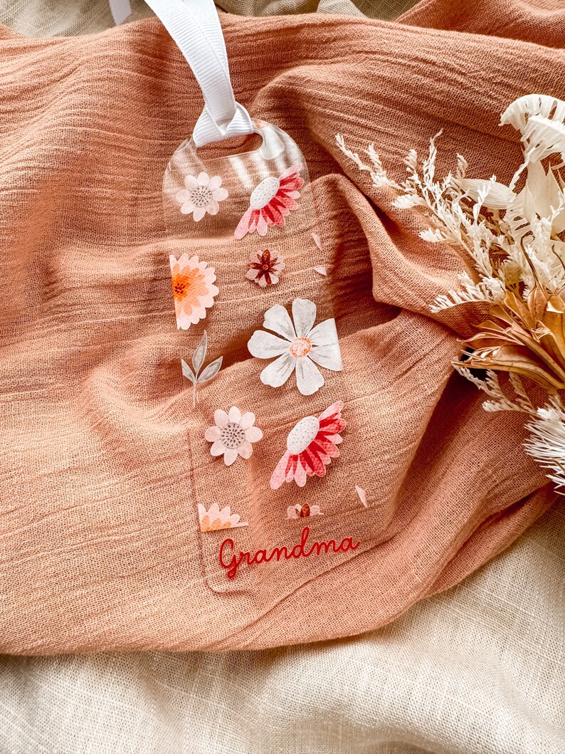 May include: A clear bookmark with a floral design and the word "Grandma" in red lettering. The bookmark is on a peach-colored fabric background.