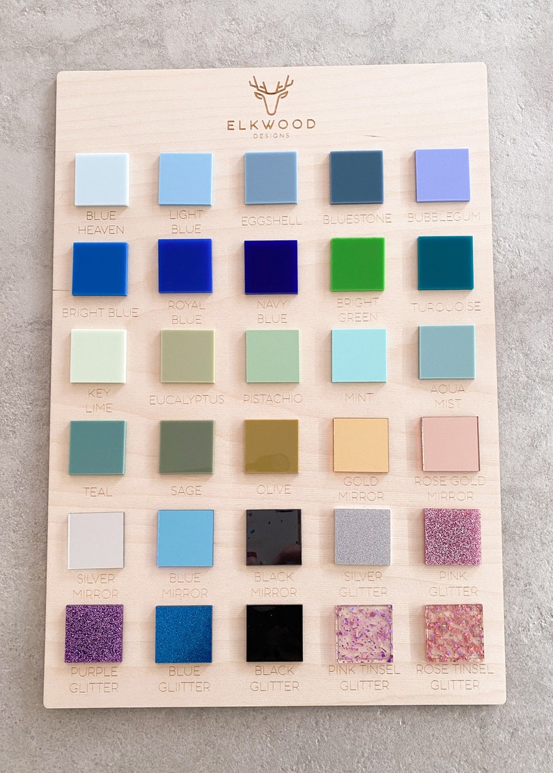 May include: A rectangular wooden display board from Elkwood Designs featuring a grid of thirty square acrylic color swatches. The samples include various shades of blue, green, gold, silver, black, and pink, with glitter, mirror, and tinsel finishes.