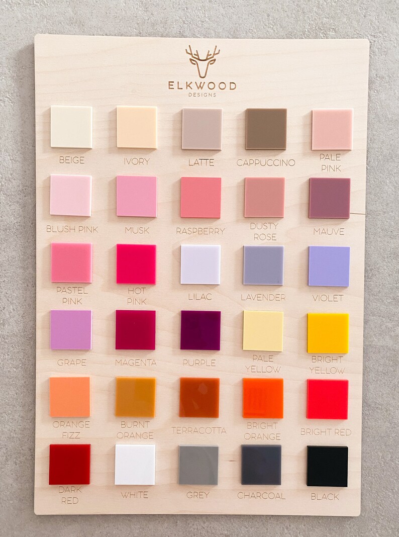May include: A wooden board displaying 25 colour swatches, each labelled with a colour name. The colours include beige, ivory, latte, cappuccino, pale pink, blush pink, musk, raspberry, dusty rose, mauve, pastel pink, hot pink, lilac, lavender, violet, grape, magenta, purple, pale yellow, bright yellow, orange fizz, burnt orange, terracotta, bright orange, bright red, dark red, white, grey, charcoal, and black.
