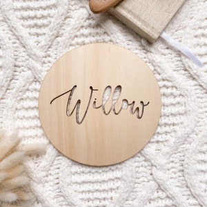 Op de afbeelding: Een rond houten bord met de naam "Willow" uitgesneden in een cursief schrift.