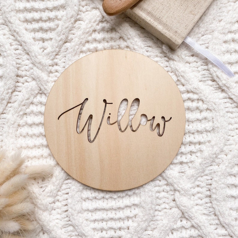 Op de afbeelding: Een rond houten bord met de naam "Willow" uitgesneden in een cursief schrift.