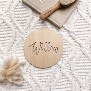 Op de afbeelding: Een ronde houten plaquette met de naam "Willow" gegraveerd in een cursief schrift. De plaquette is lichtbruin en heeft een natuurlijke houtnerf.