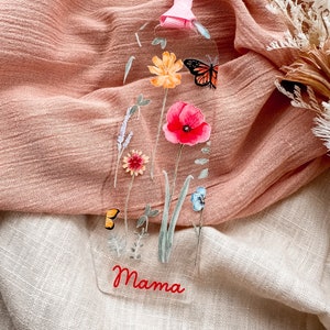 May include: A clear bookmark with a floral design featuring a butterfly, poppy, and other flowers. The bookmark has the word "Mama" written in red at the bottom.