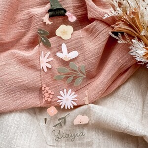May include: A clear plastic bookmark with a floral design and the name "Yiavjia" written in cursive. The bookmark has a green ribbon attached to the top.