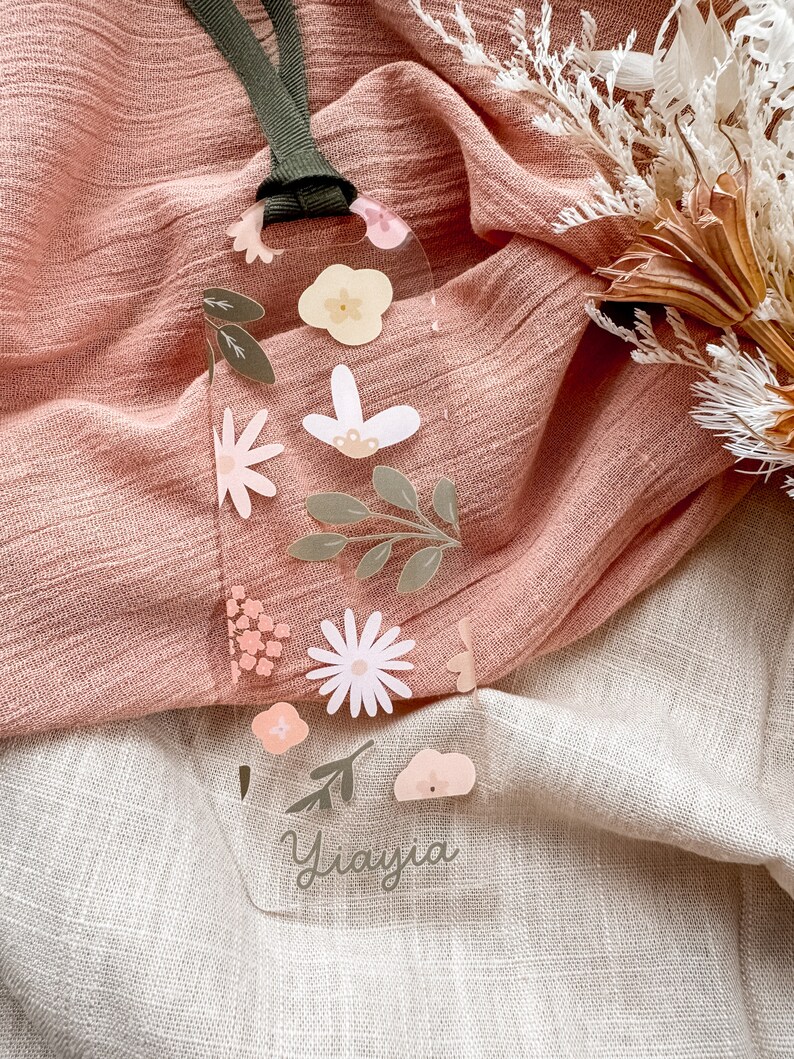 May include: A clear plastic bookmark with a floral design and the name "Yiavjia" written in cursive. The bookmark has a green ribbon attached to the top.