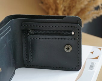 May include: A black leather wallet with a zippered pocket and a snap closure. The wallet is open and the inside is visible.