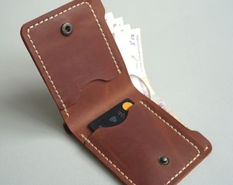 May include: A brown leather wallet with a white stitch detail and two snap closures. The wallet is open and shows a credit card and some bills inside.