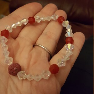 May include: A red and clear crystal bracelet with a lava rock bead. The bracelet is made with faceted crystal beads and red glass beads.