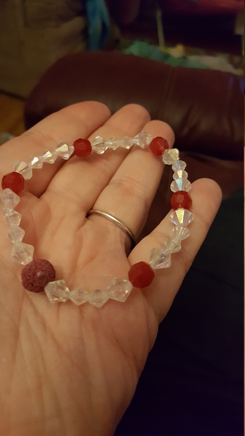 May include: A red and clear crystal bracelet with a lava rock bead. The bracelet is made with faceted crystal beads and red glass beads.