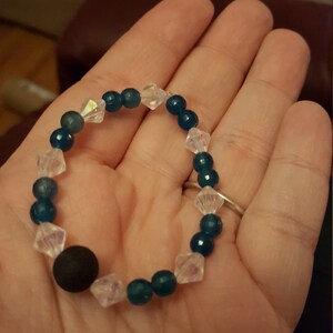 May include: A teal and clear beaded bracelet with a black bead. The bracelet is made with round beads and faceted clear beads.