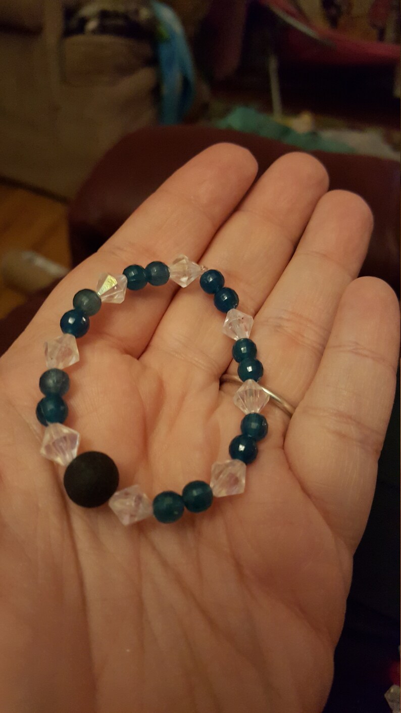 May include: A teal and clear beaded bracelet with a black bead. The bracelet is made with round beads and faceted clear beads.