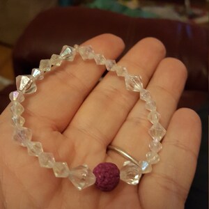 May include: A bracelet made of clear iridescent beads with a single dark purple bead in the centre.
