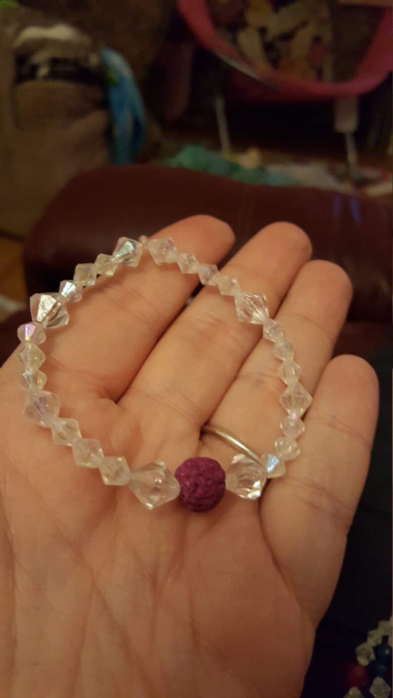 May include: A bracelet made of clear iridescent beads with a single dark purple bead in the centre.