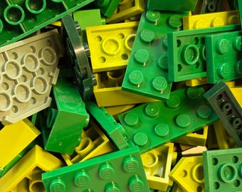 May include: A close-up shot of a pile of colorful building blocks in shades of green, yellow, and gray. The blocks are of various shapes and sizes, including rectangular and square pieces with circular studs. The image showcases a variety of Lego bricks.