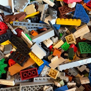 May include: A large, jumbled collection of plastic building bricks in various shapes, sizes, and colors including red, blue, yellow, green, brown, black, white, and gray. The assortment features rectangular blocks, flat plates, and gears.
