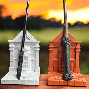 May include: Two wizard wands, black and brown, presented on miniature building stands. The stands are grey and orange, with the text "INNOVATIVE WIZARD SINCE 2019". The wands are set against a sunset backdrop.