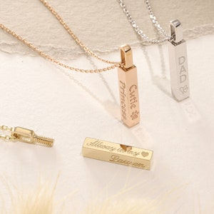 May include: Three vertical bar pendant necklaces in rose gold, silver, and gold tones. The rose gold pendant is engraved with "Cutie Princess" and a paw print. The silver pendant is engraved with "DAD" and a heart. The gold pendant reads "Always in my heart" and "Lauren".