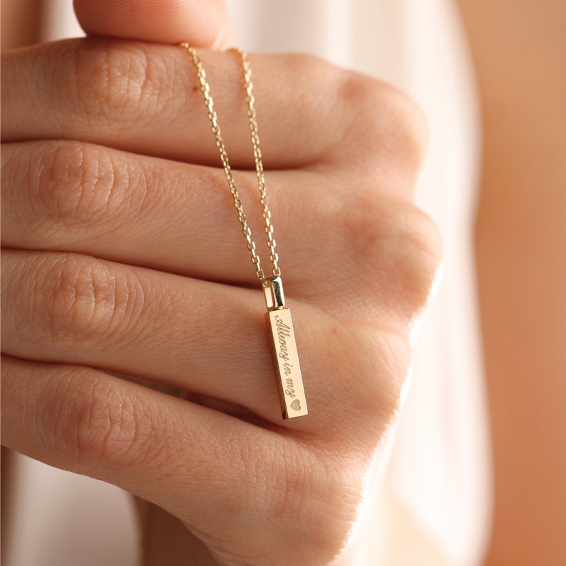 May include: A gold-toned vertical bar pendant necklace featuring a delicate chain. The rectangular bar is engraved with the text "Always in my" followed by a small heart symbol. The piece has a polished metallic finish and a simple link chain.