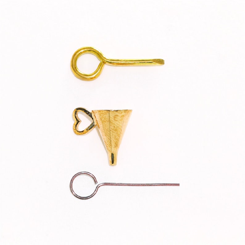 May include: Three gold-toned jewelry findings: a jump ring with a straight pin, a cone-shaped bead with a heart-shaped loop, and a jump ring with a straight pin.