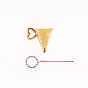 May include: A gold-coloured metal funnel featuring a small heart-shaped handle on the side, accompanied by a thin, straight metal rod with a circular loop at one end. The funnel has a wide, open top and a narrow, tapered bottom opening.