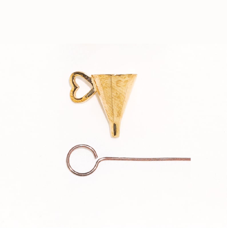 May include: A gold-coloured metal funnel featuring a small heart-shaped handle on the side, accompanied by a thin, straight metal rod with a circular loop at one end. The funnel has a wide, open top and a narrow, tapered bottom opening.