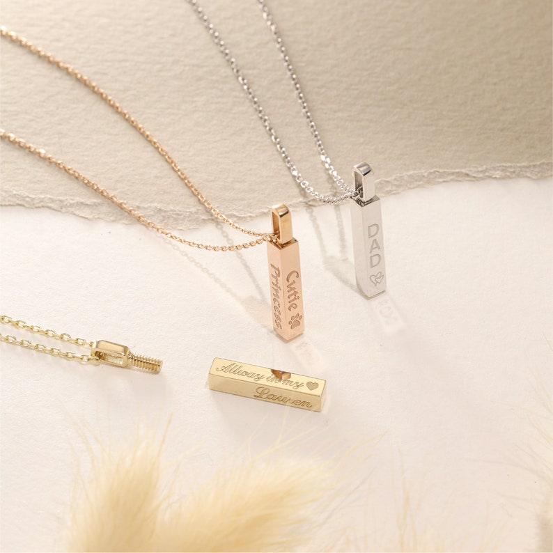 May include: Three vertical bar pendant necklaces in rose gold, silver, and gold tones. The rose gold pendant is engraved with "Cutie Princess" and a paw print. The silver pendant is engraved with "DAD" and a heart. The gold pendant reads "Always in my heart" and "Lauren".