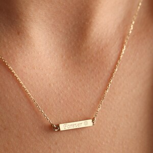 May include: A gold chain necklace with a small bar pendant that says "Forever" with a sun symbol.