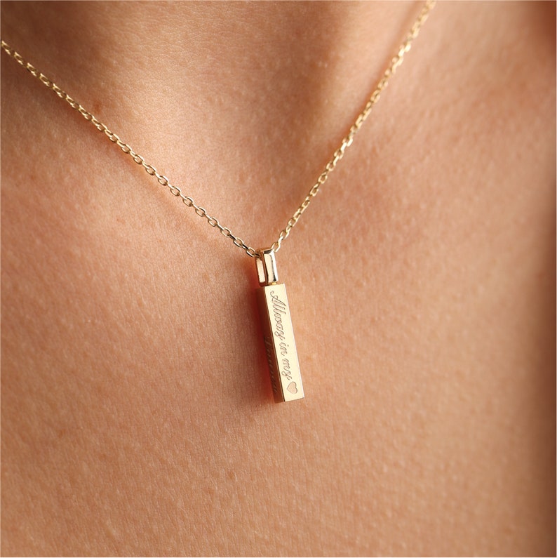 May include: A gold-toned vertical bar pendant necklace featuring a delicate chain and an engraved inscription that reads Always in my heart with a small heart symbol at the end of the text, suspended from a thin, polished gold-coloured metal chain.