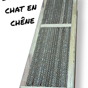 Peut inclure: Un griffoir rectangulaire pour chat en carton ondulé et encadré de bois clair. Le texte "Griffoir Chat en Chêne" est imprimé sur le côté. La surface à griffer est constituée de bandes de carton verticales.