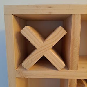 Puede incluir: Un estante de vino de madera con un dise&ntilde;o en forma de cruz para guardar botellas de vino. El estante est&aacute; hecho de madera natural y tiene un color marr&oacute;n claro.