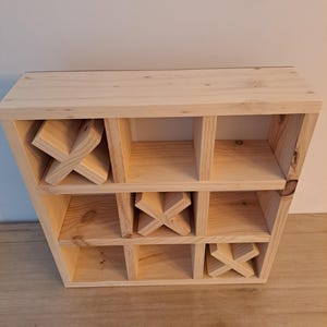 Puede incluir: Un juego de tres en raya de madera con nueve compartimentos. El juego est&aacute; hecho de madera sin terminar y tiene tres piezas en forma de X en su lugar.