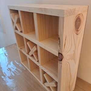 Puede incluir: Una estanter&iacute;a de madera con un dise&ntilde;o de tres en raya. La estanter&iacute;a est&aacute; hecha de madera natural y tiene nueve compartimentos.