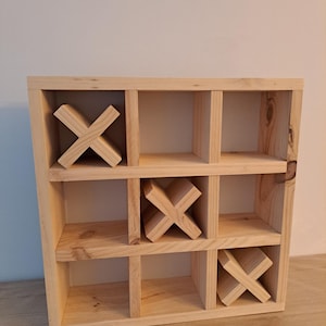 Puede incluir: Un juego de tres en raya de madera con nueve compartimentos. El juego est&aacute; hecho de madera natural y tiene tres piezas de madera en forma de X.