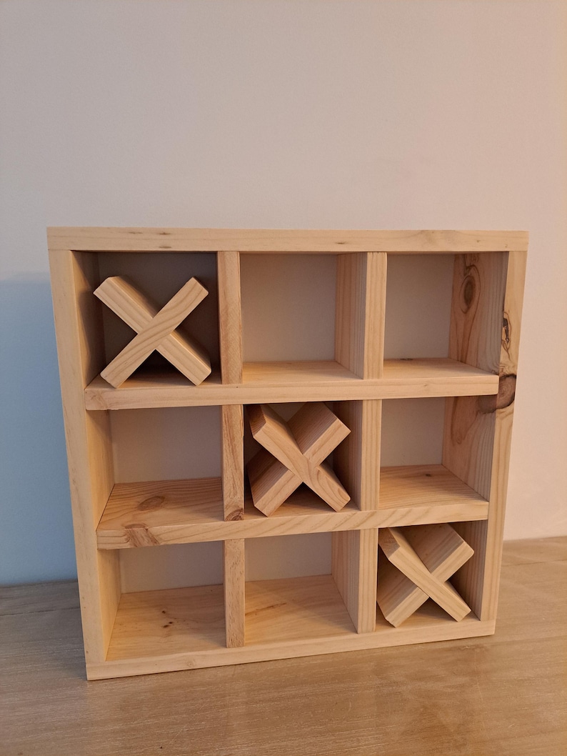 Puede incluir: Un juego de tres en raya de madera con nueve compartimentos. El juego est&aacute; hecho de madera natural y tiene tres piezas de madera en forma de X.