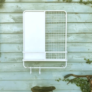 Puede incluir: Organizador de pared de metal blanco con un panel s&oacute;lido y una secci&oacute;n de rejilla. Cuenta con un estante, una barra para toallas y dos ganchos. Montado en una pared de madera azul claro.