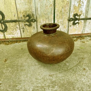 May include: A large, round, brown metal vase with a slightly flared opening. The vase has a textured surface and appears to be antique.