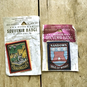 May include: Two Glenthorne Series woven souvenir badges in original packaging. One badge features a Shanklin landscape with a house and trees. The other badge displays a Sandown Isle of Wight crest with a red arch, blue water, and three white birds.